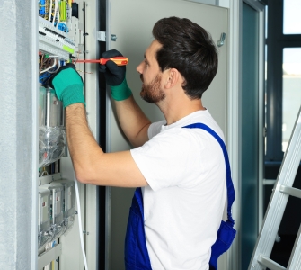 Electrician repairing fuse box with screwdriver indoors