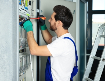 Electrician repairing fuse box with screwdriver indoors