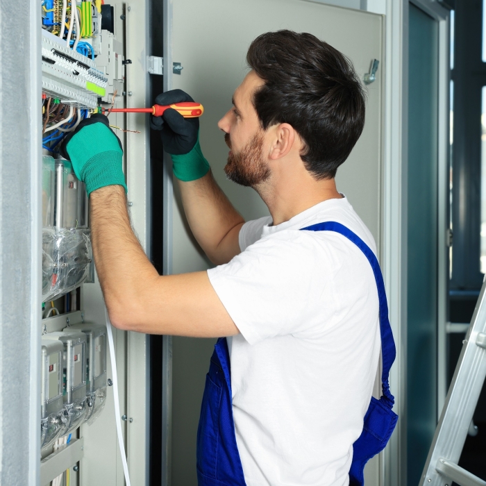 Electrician repairing fuse box with screwdriver indoors