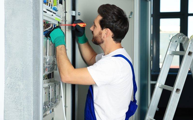 Electrician repairing fuse box with screwdriver indoors