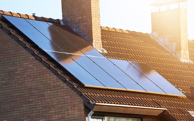 Close-up of rooftop solar panels and chimney. Residential house with solar panels on roof. Solar energy